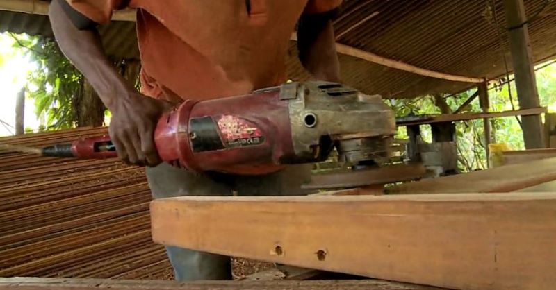 A person is holding a large piece of machinery, grinding a piece of wood