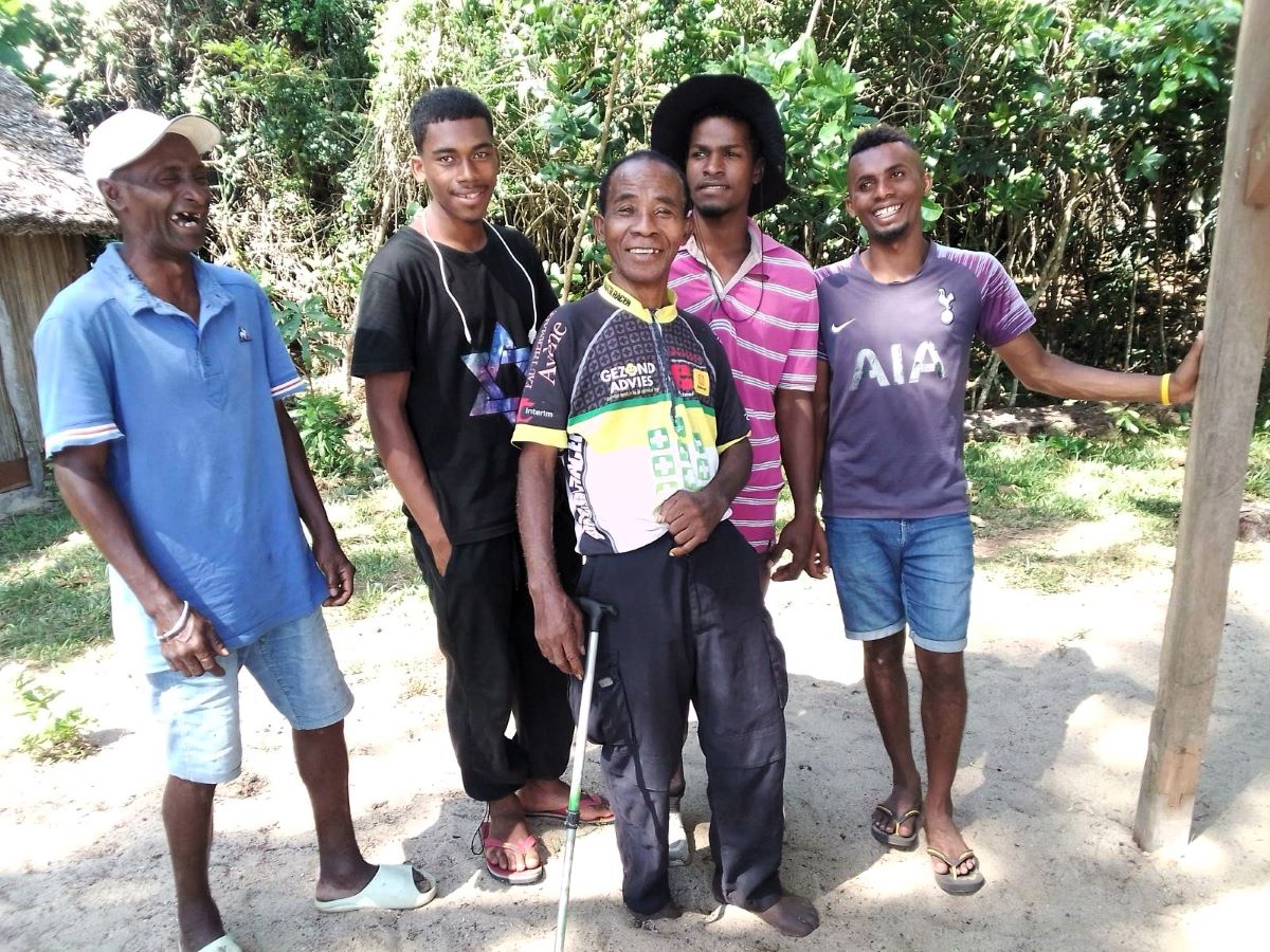 Five men are standing together in a clearing in the forest, all smiling broadly and looking very happy